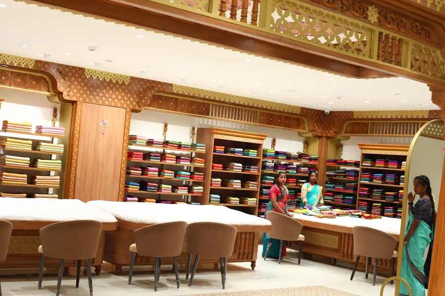 The saree hall: carved wooden shelving running the full height of the walls, packed with folded silks in every colour, with counter seating along the middle.