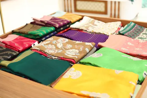 Silk sarees fanned out on a counter in emerald, magenta, mustard, purple and gold zari.