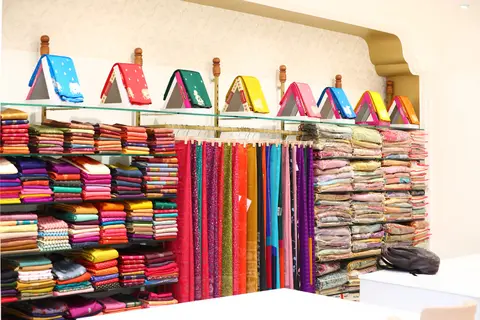 A wall of sarees on display with samples hung above stacked shelves.